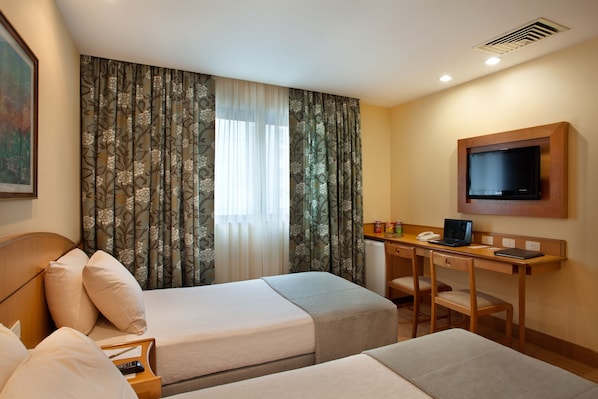 A hotel room with two beds, a desk with a laptop, a television, and a small refrigerator. - Windsor Martinique Copacabana (Rio de Janeiro)