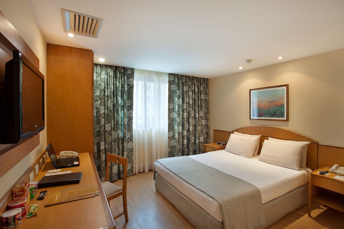 Ein Hotelzimmer mit Bett, Schreibtisch, Stuhl, Fernseher und einem Bild an der Wand.