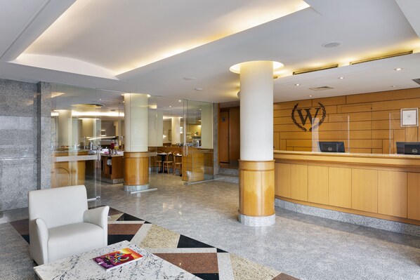 A modern hotel lobby with a reception desk, seating area, and a glass partition separating the lobby from the dining area. - Windsor Martinique Copacabana (Rio de Janeiro)