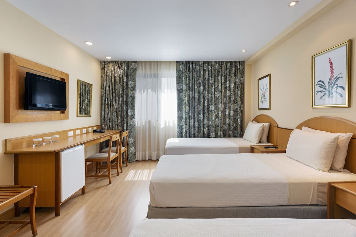 Ein Hotelzimmer mit zwei Betten, einem Schreibtisch mit Fernseher und einem kleinen Kühlschrank.