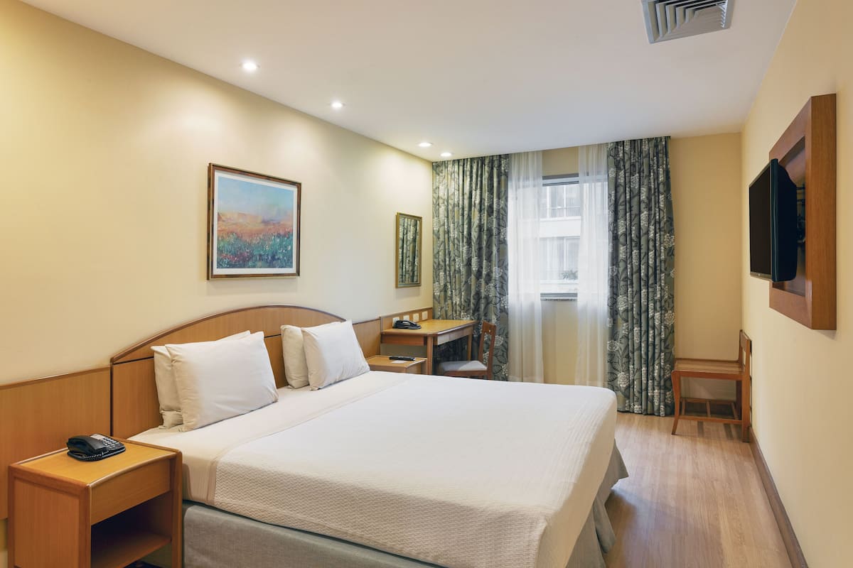 Ein Hotelzimmer mit einem großen Bett, einem Schreibtisch, einem Sessel, einem Telefon und einem Fernseher.