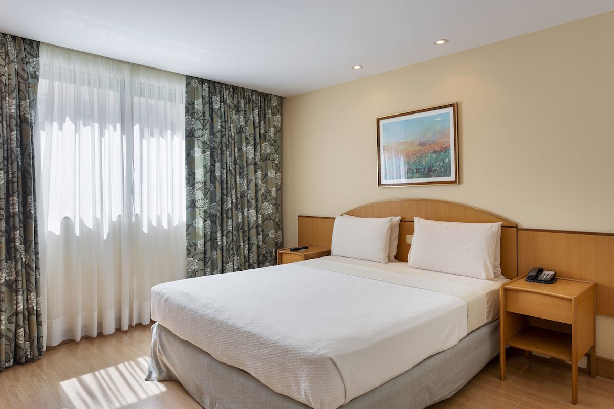 Ein Hotelzimmer mit einem großen Bett, einem hölzernen Kopfteil, einem Nachttisch mit Telefon und einem Bild an der Wand.