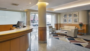 A reception area with a wooden counter, a white sofa, and a coffee table. - Windsor Martinique Copacabana (Rio de Janeiro)