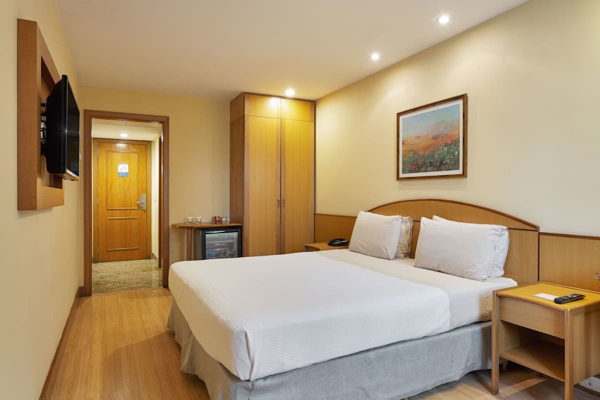 Ein Hotelzimmer mit Bett, Nachttisch, Fernseher, Tür und einem Bild an der Wand.