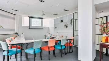 A modern meeting room with a long table, colorful chairs, a projector screen, and a whiteboard.