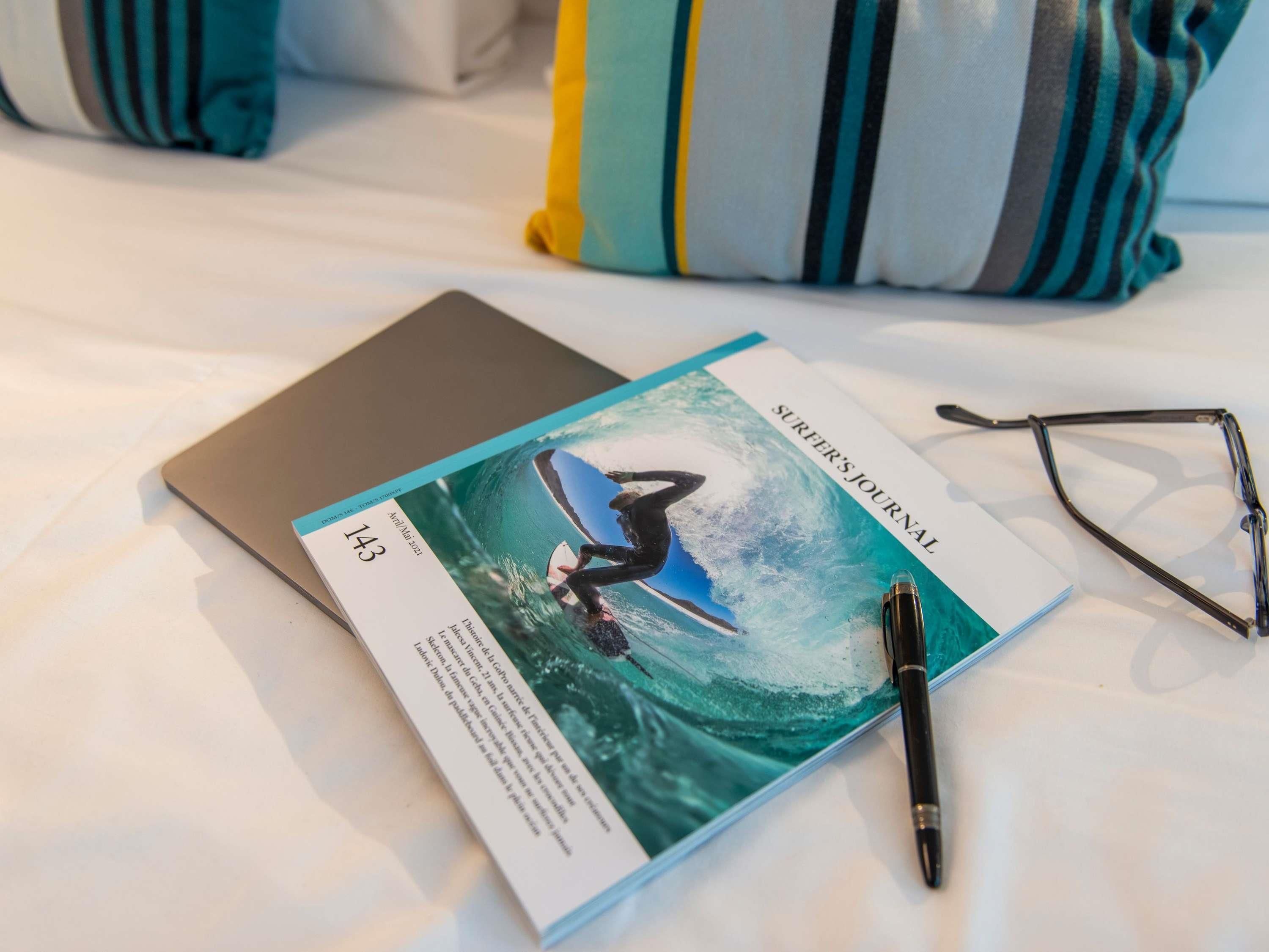 A laptop, a pen, and a pair of glasses on a bed with a striped pillow.