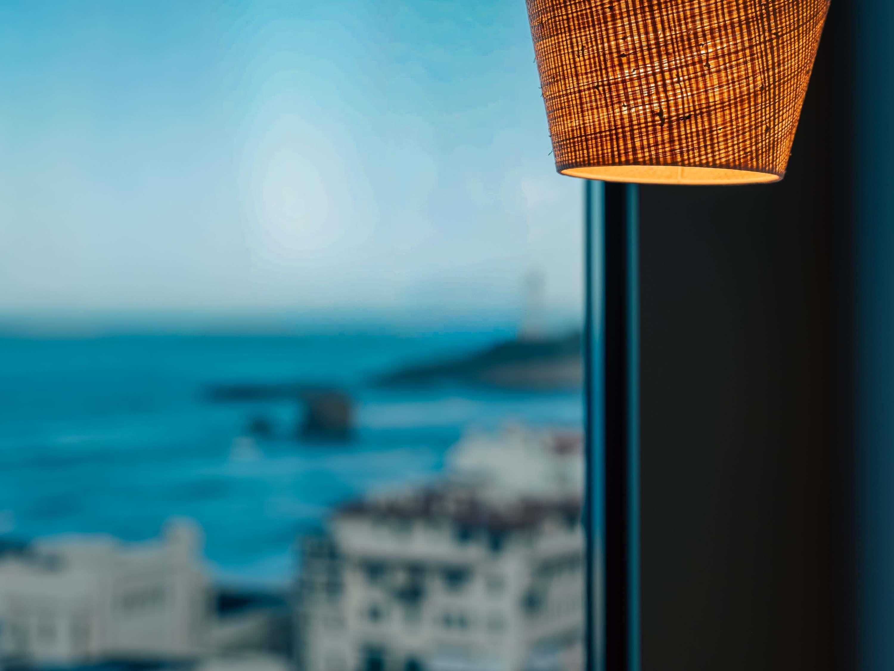 A close-up of a woven lamp shade with a blurred coastal cityscape in the background.
