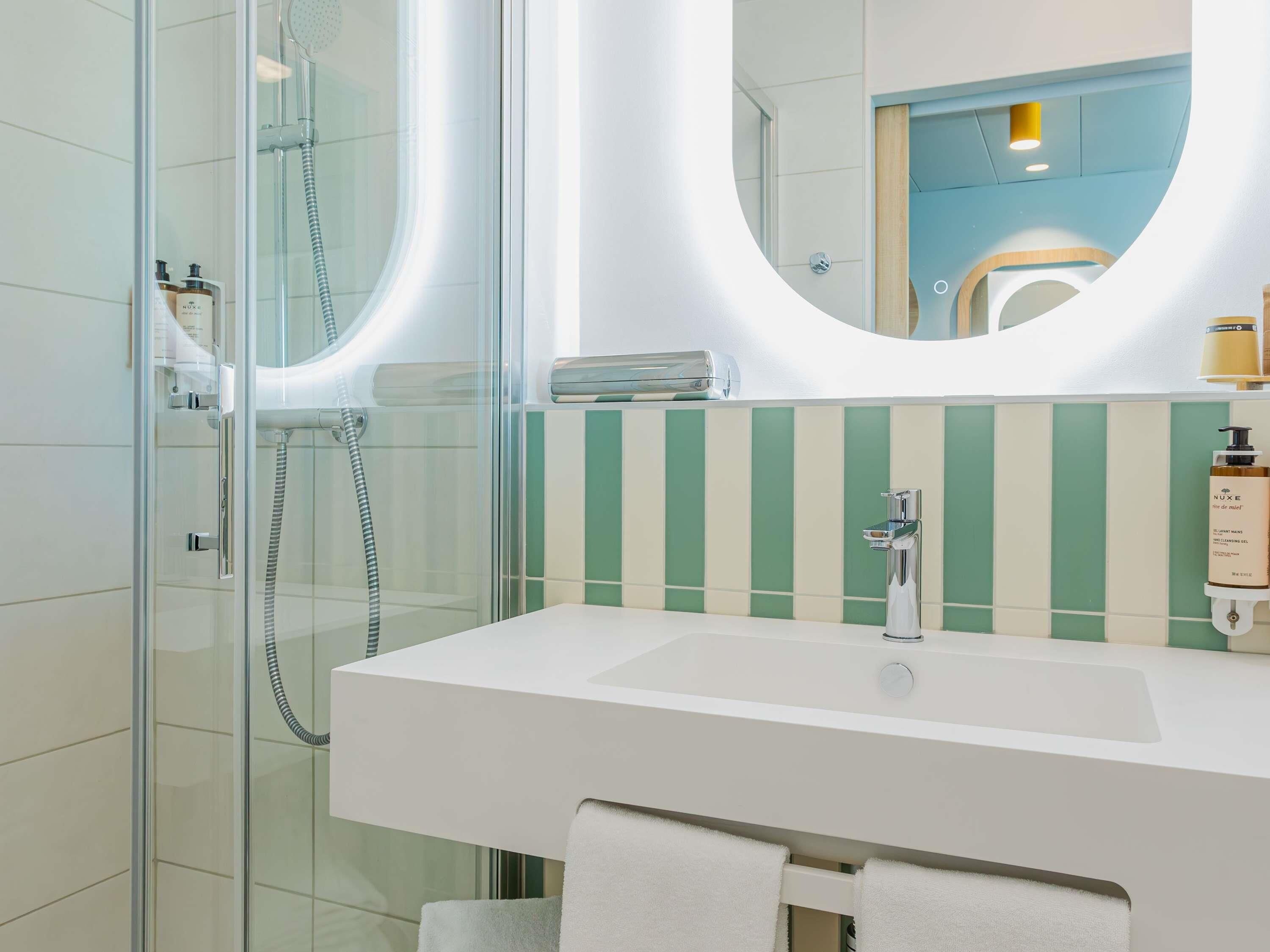 Une salle de bain moderne avec une douche à parois de verre, un lavabo blanc et un miroir doté d’un cadre circulaire.