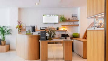 Un mostrador de recepción con una computadora, una impresora y una planta. Hay una pantalla montada en la pared sobre el mostrador.