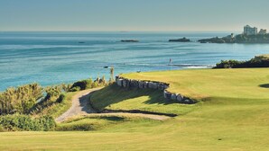 A coastal golf course with a clear view of the ocean, a stone wall, and a path leading to the water.