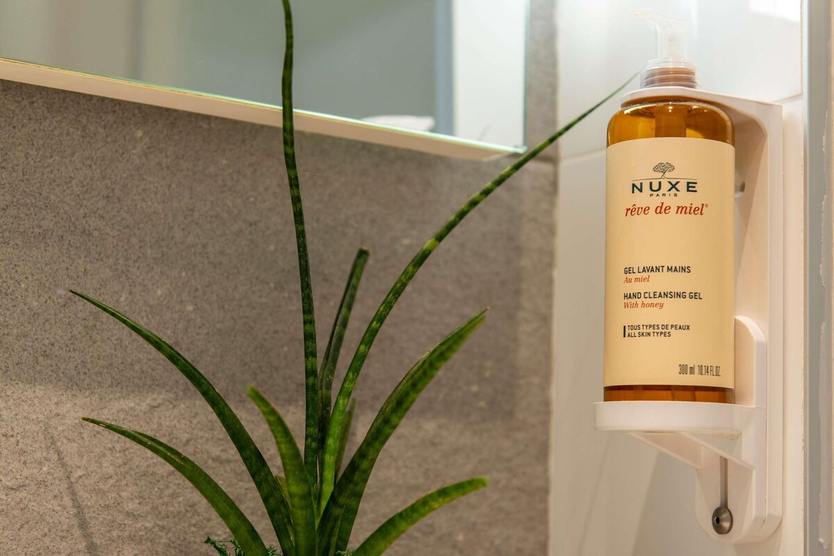 A hand cleansing gel bottle labeled 'NUXE PARIS' with a pump dispenser, placed on a white surface next to a potted plant.
