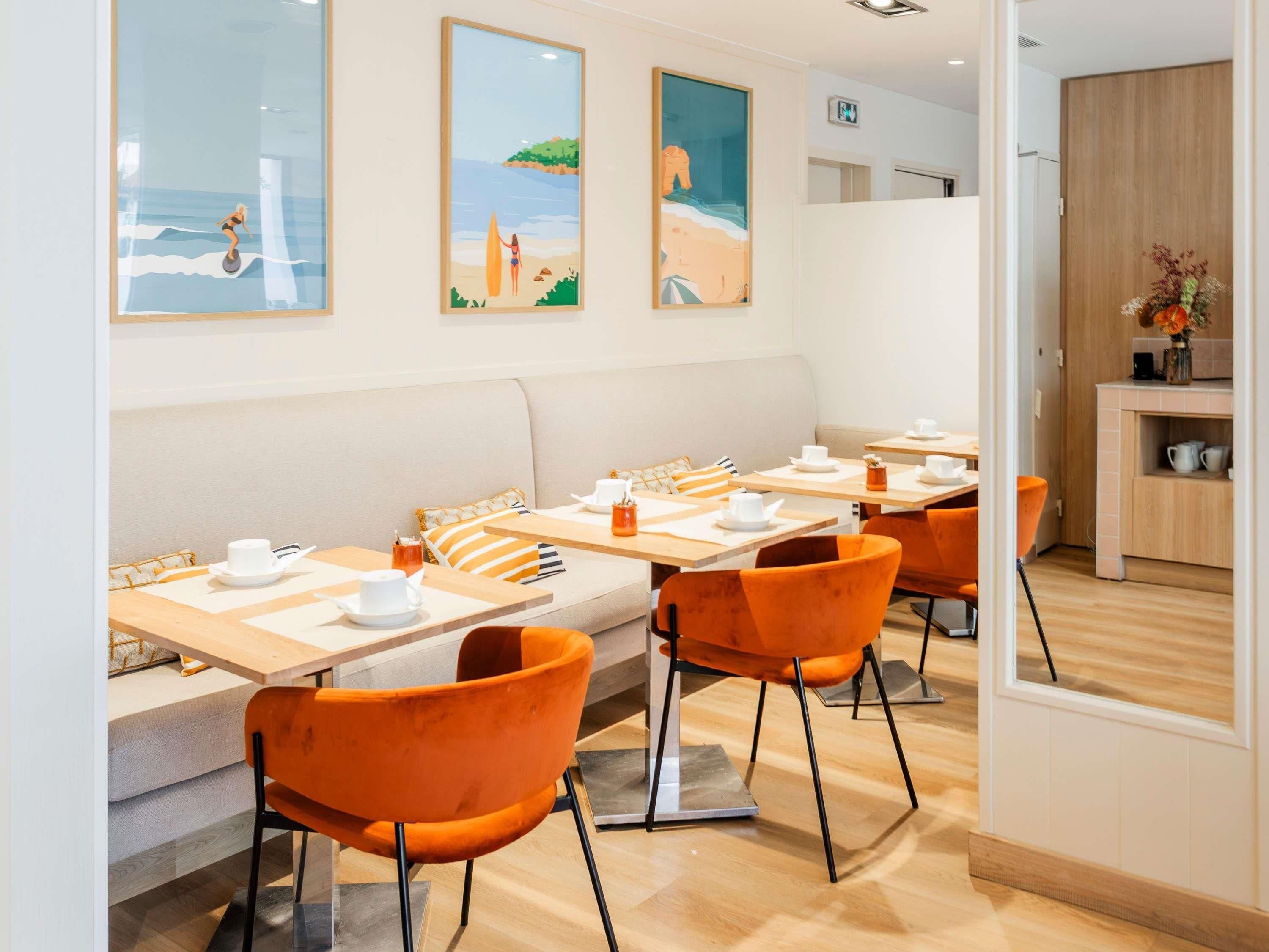A modern dining area with wooden tables, orange chairs, and a sofa.