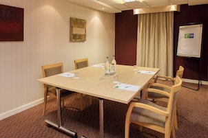 Un salón de conferencias con una mesa, sillas, una pizarra y una cortina.
