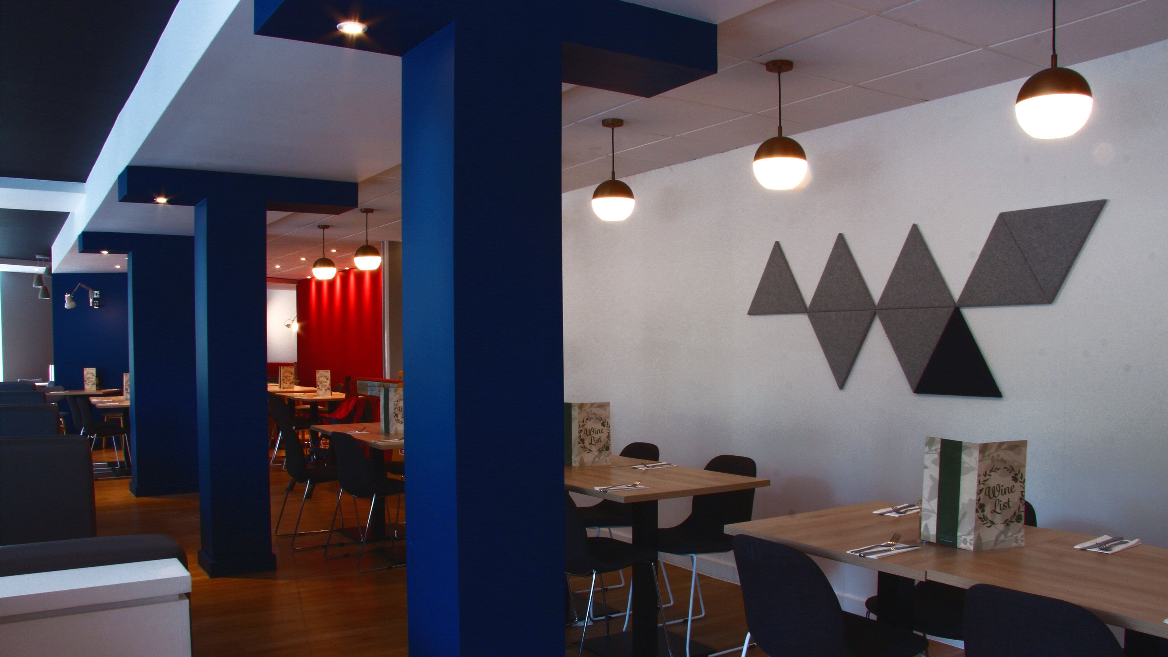 A modern dining area with tables and chairs, pendant lighting, and a wall with geometric wall art.