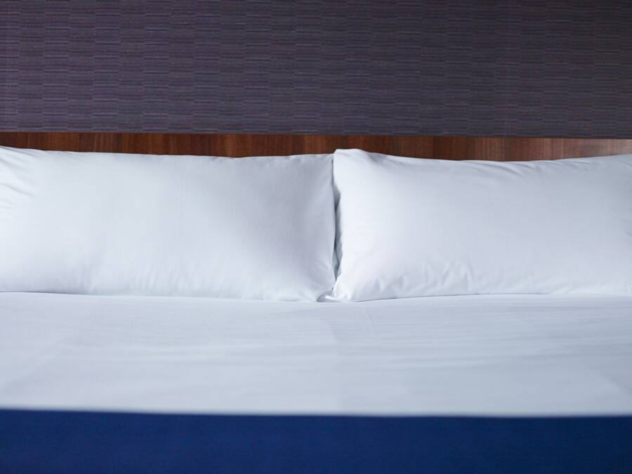 A neatly made bed with white linens and a wooden headboard.