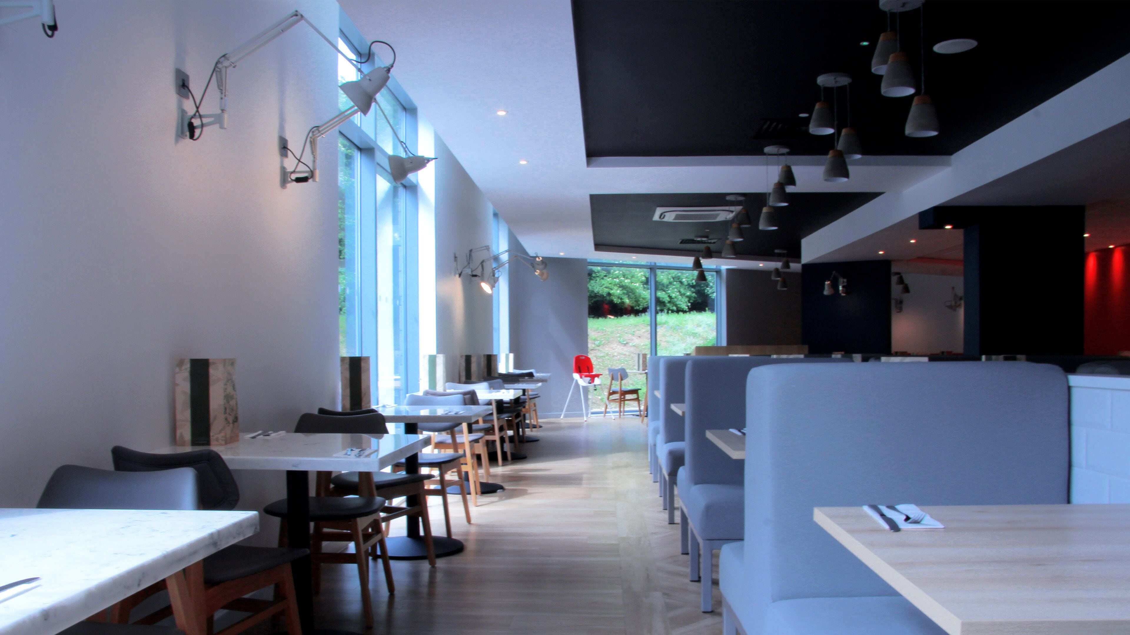Een modern restaurantinterieur met hoge tafels en zitjes, grote ramen en hanglampen.