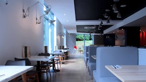 Un intérieur de restaurant moderne avec des tables hautes et des banquettes, de grandes fenêtres et des luminaires suspendus.