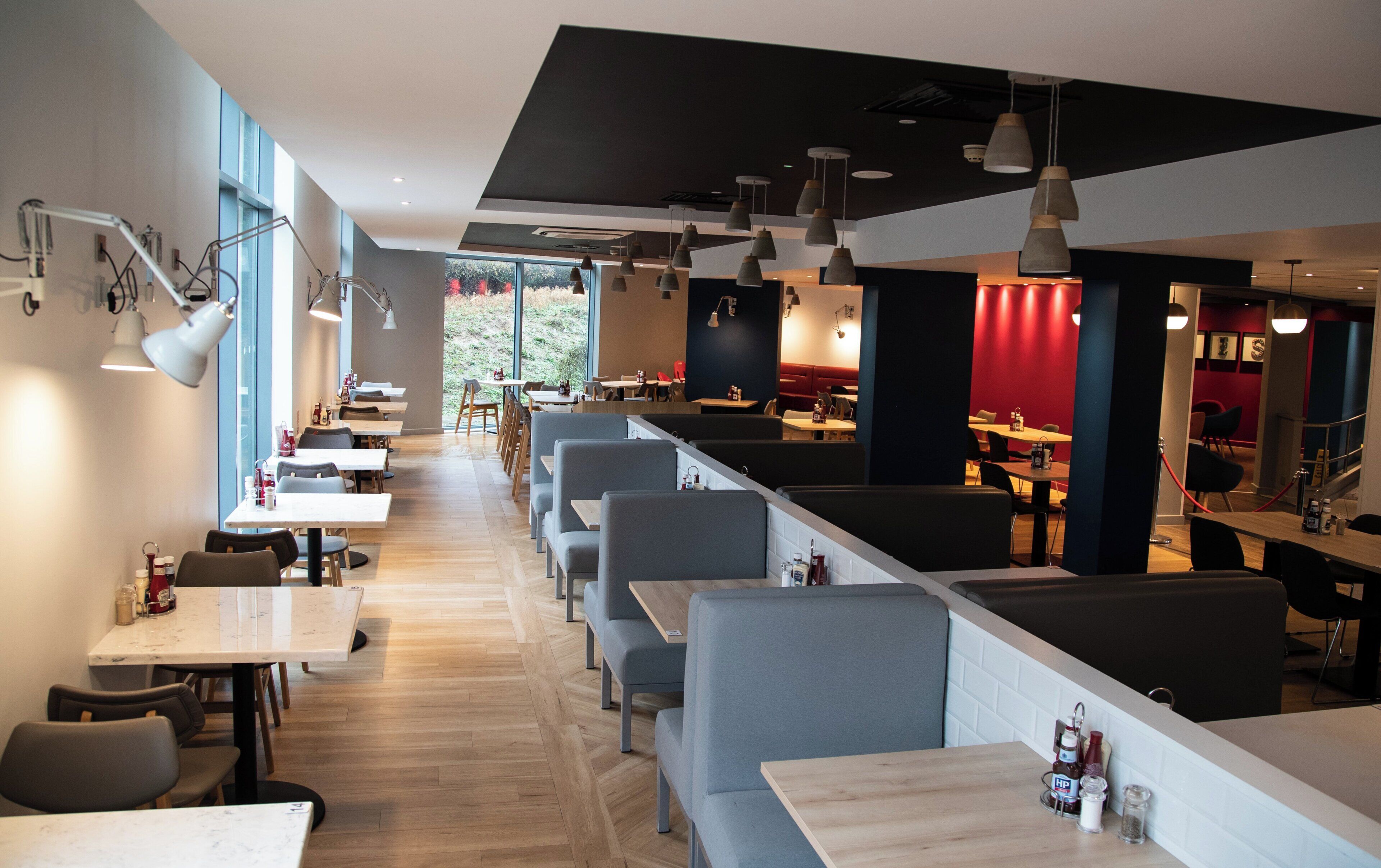 Un ristorante moderno con tavoli alti e banconi, illuminazione a sospensione e vista su una zona verde esterna.
