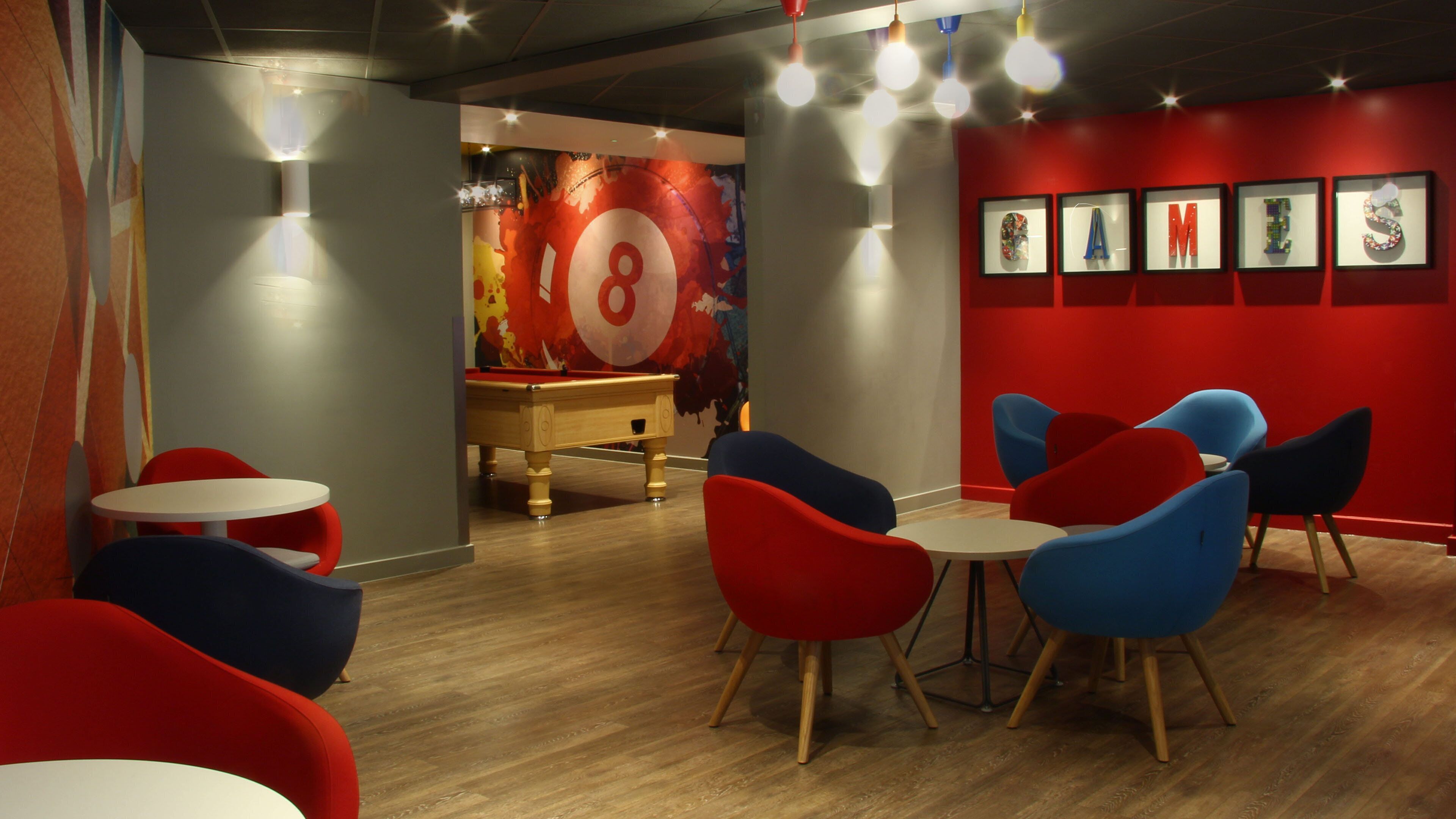 A room with a pool table, red and blue chairs, and a red wall with framed pictures.
