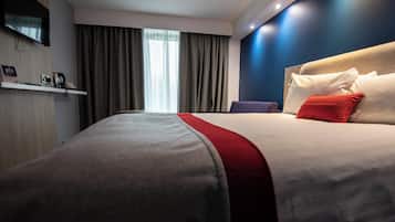 Una habitación de hotel con una cama grande, un televisor de pantalla plana montado en la pared y una ventana con cortinas.