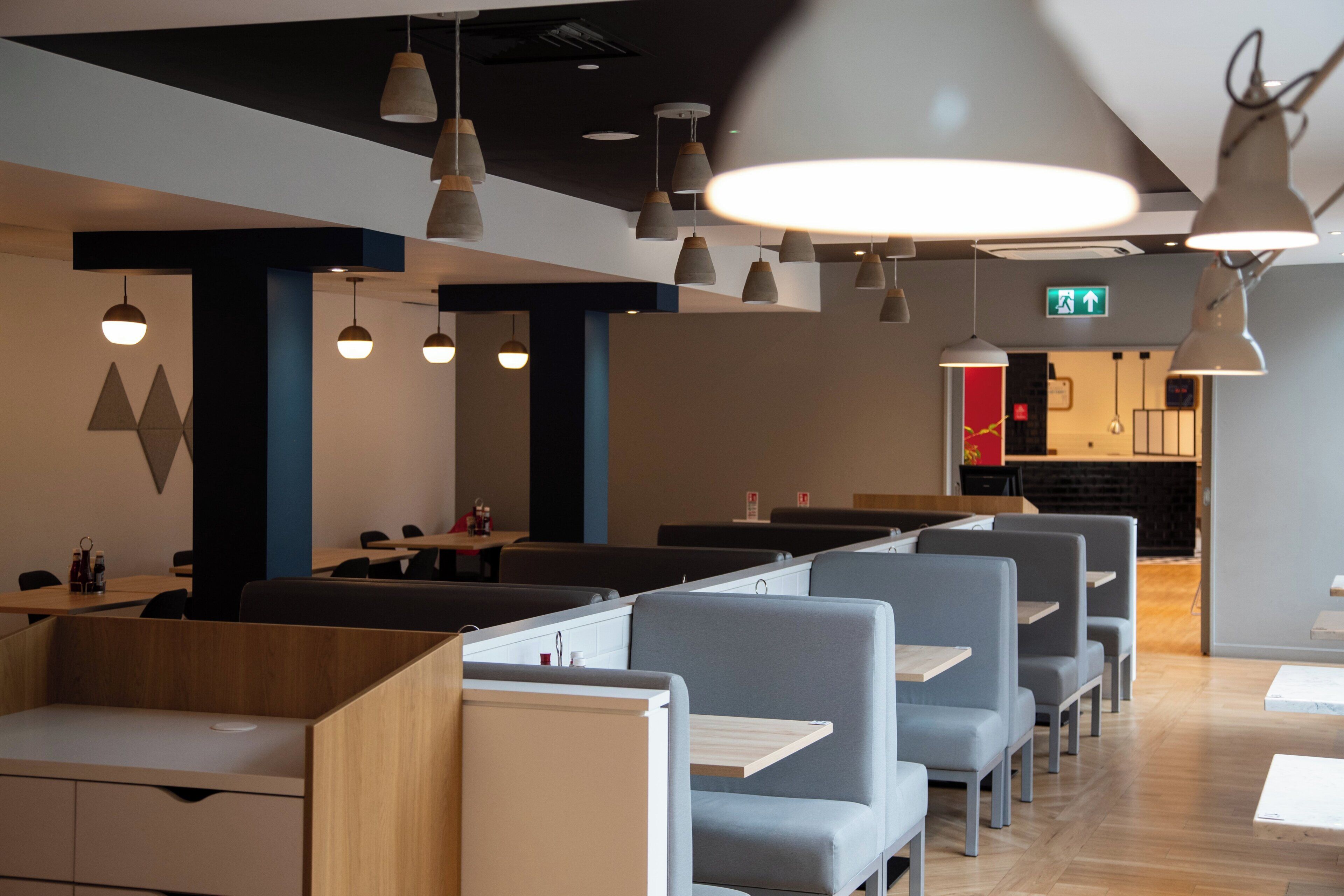 A modern restaurant interior with high tables and booths, pendant lighting, and a visible exit sign.
