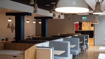 A modern restaurant interior with high tables and booths, pendant lighting, and a visible exit sign.