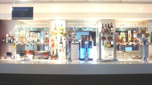 Un espace bar équipé de plusieurs distributeurs de boissons, d’un panneau indiquant que seules les commandes de boissons y sont acceptées, ainsi que d’une variété de bouteilles et de verres.