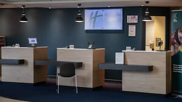 A reception desk area with a digital screen displaying 'Holiday Inn Express' branding, a cash machine, and a sign asking if guests have parked in the car park.
