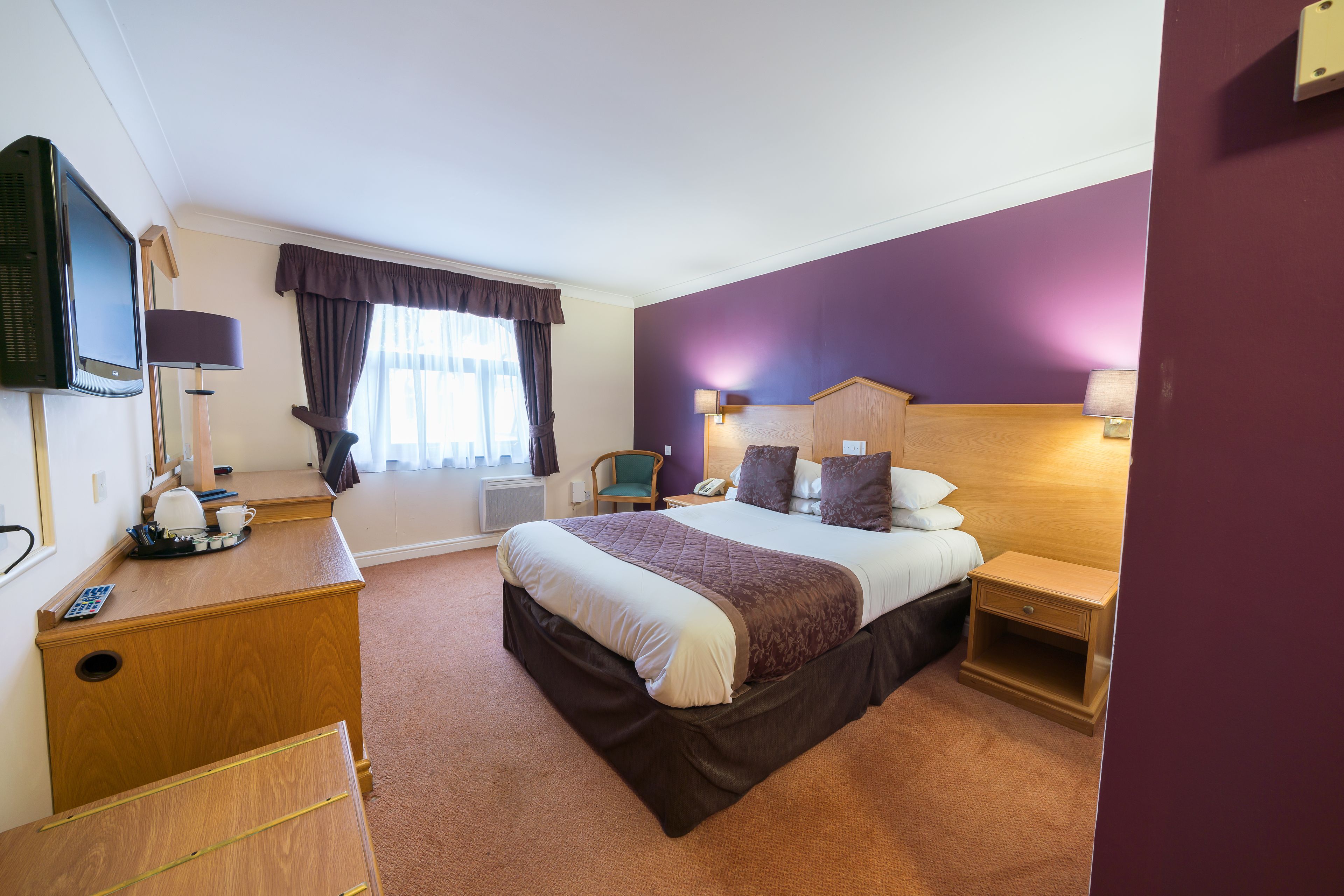A hotel room with a bed, bedside table, lamp, and a desk with a telephone and a coffee maker.