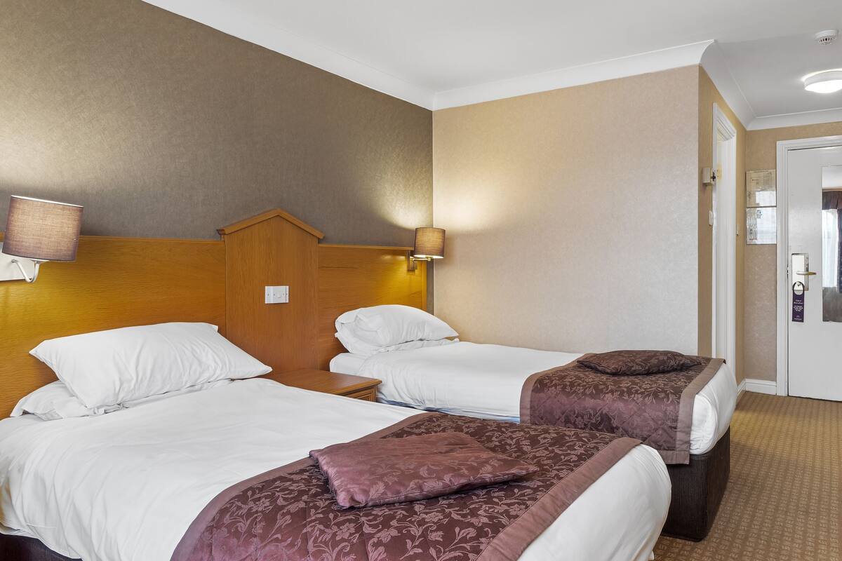 Una habitació d'hotel amb dos llits, cadascun amb roba de llit blanca i un capçal marró. Hi ha làmpades muntades a la paret als costats dels llits.