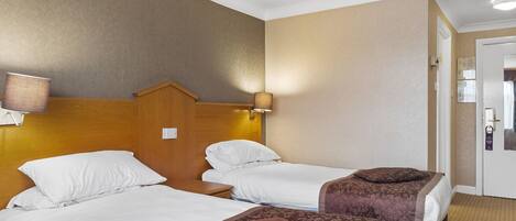Habitación de hotel con dos camas, cada una con ropa blanca y cabeceros marrones. Hay lámparas de pared a cada lado de las camas.