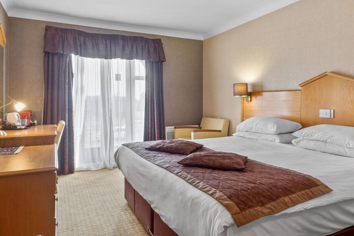 Una habitació d'hotel amb un llit, un escriptori amb una làmpada i una cadira.