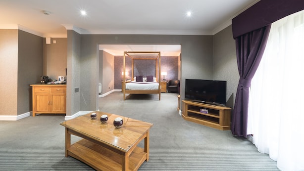 Una habitación de hotel con una cama, televisión, una mesa de madera y un armario.