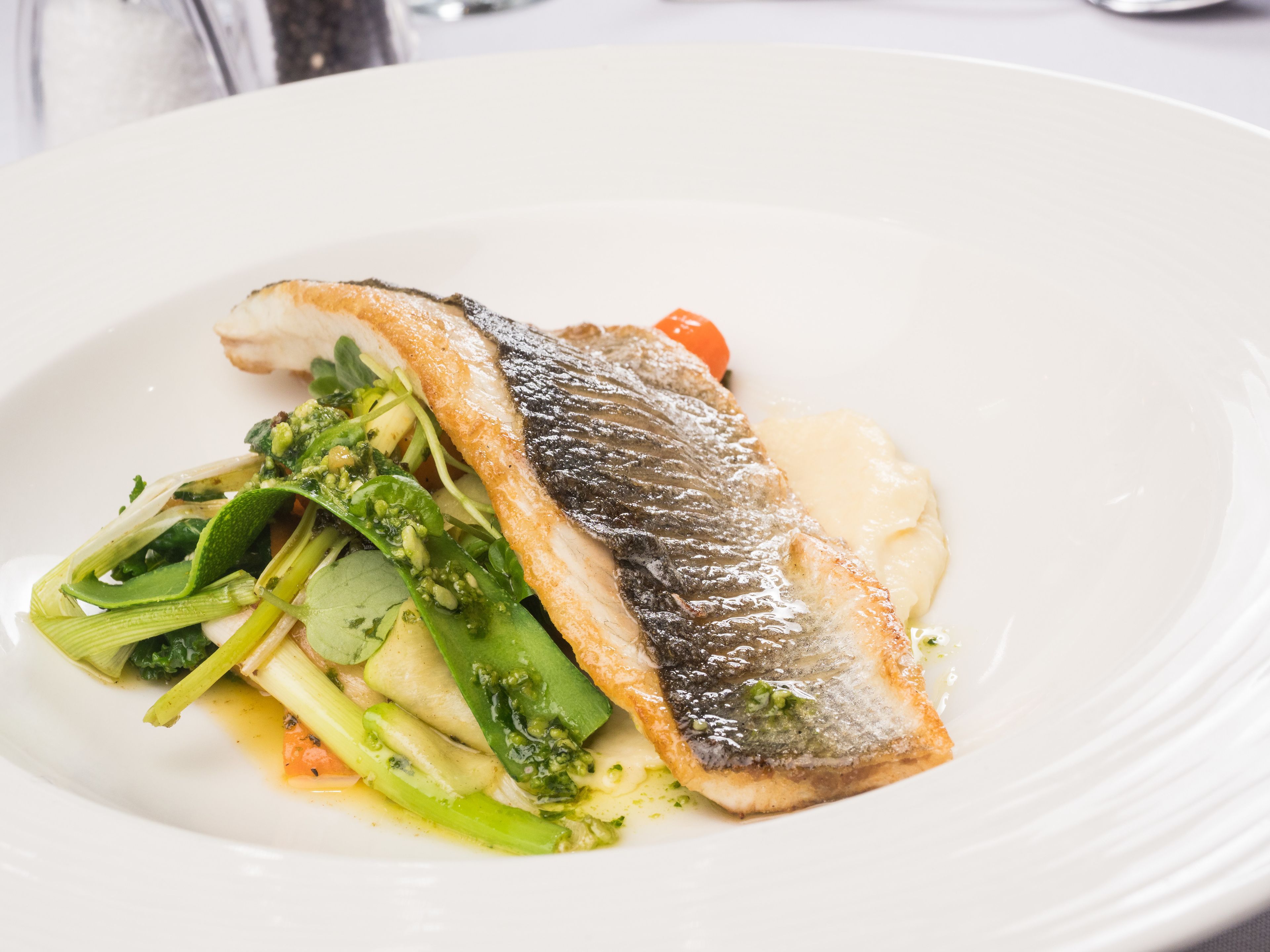 Un plato blanco con un trozo de pescado, verduras y una porción de salsa.