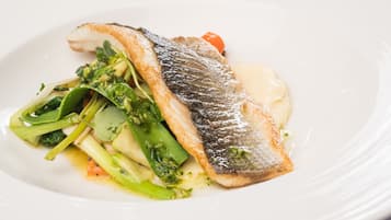Un plato blanco con un trozo de pescado, verduras y una porción de salsa.
