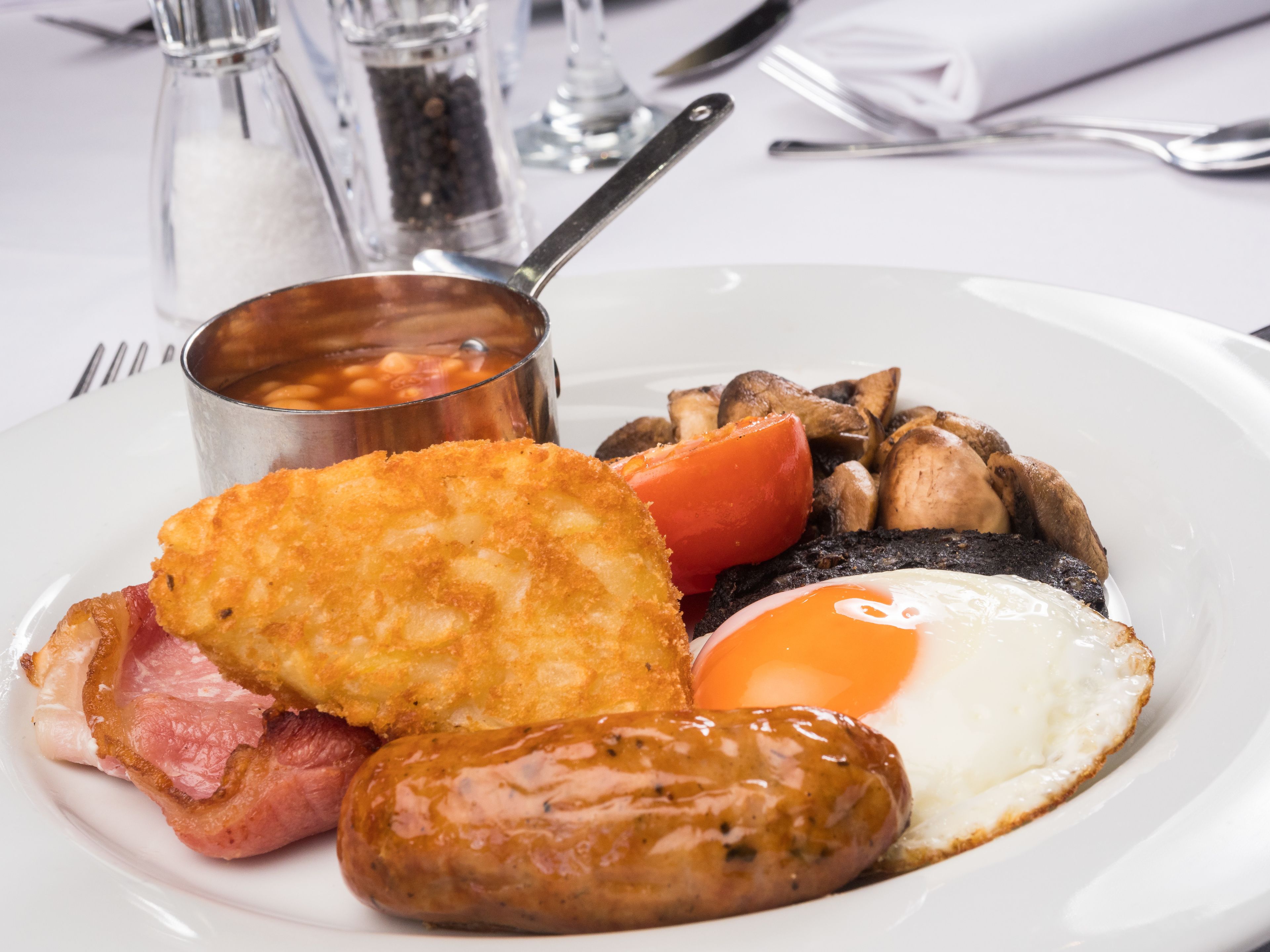 A plate of breakfast food including eggs, sausages, bacon, mushrooms, and a fried patty.
