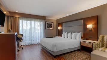 A hotel room with a large bed, a desk, a chair, a TV, and a window with curtains.