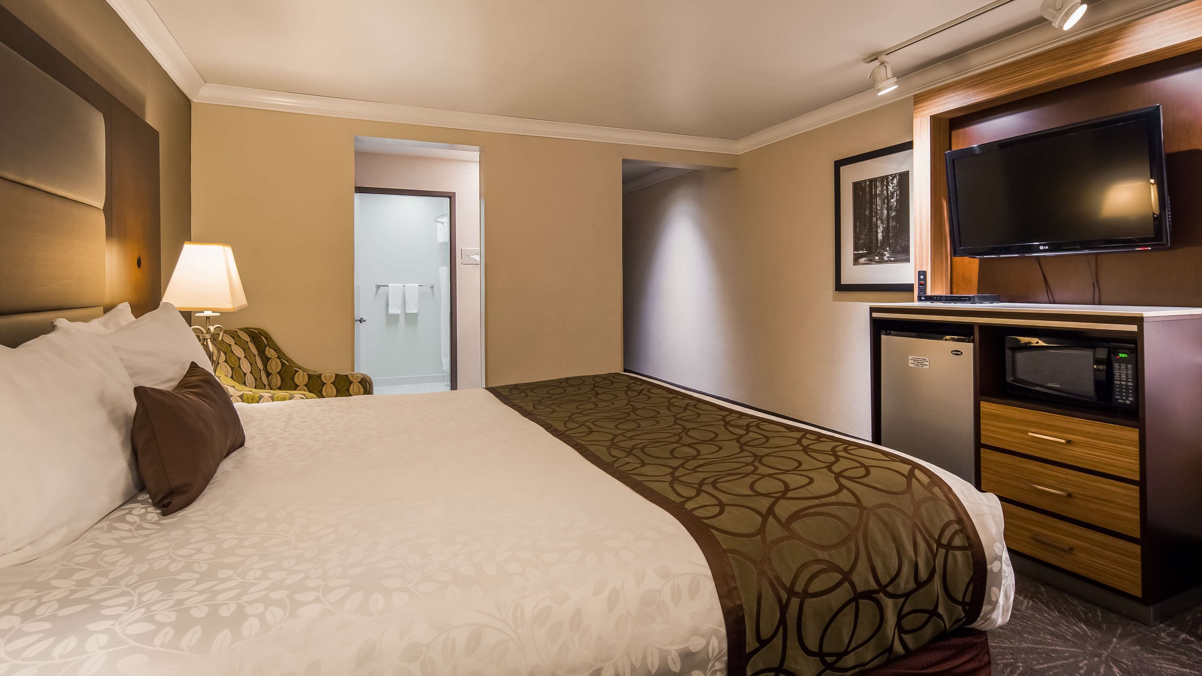 A hotel room with a bed, a desk with a microwave, a television, and a bathroom visible through an open door.