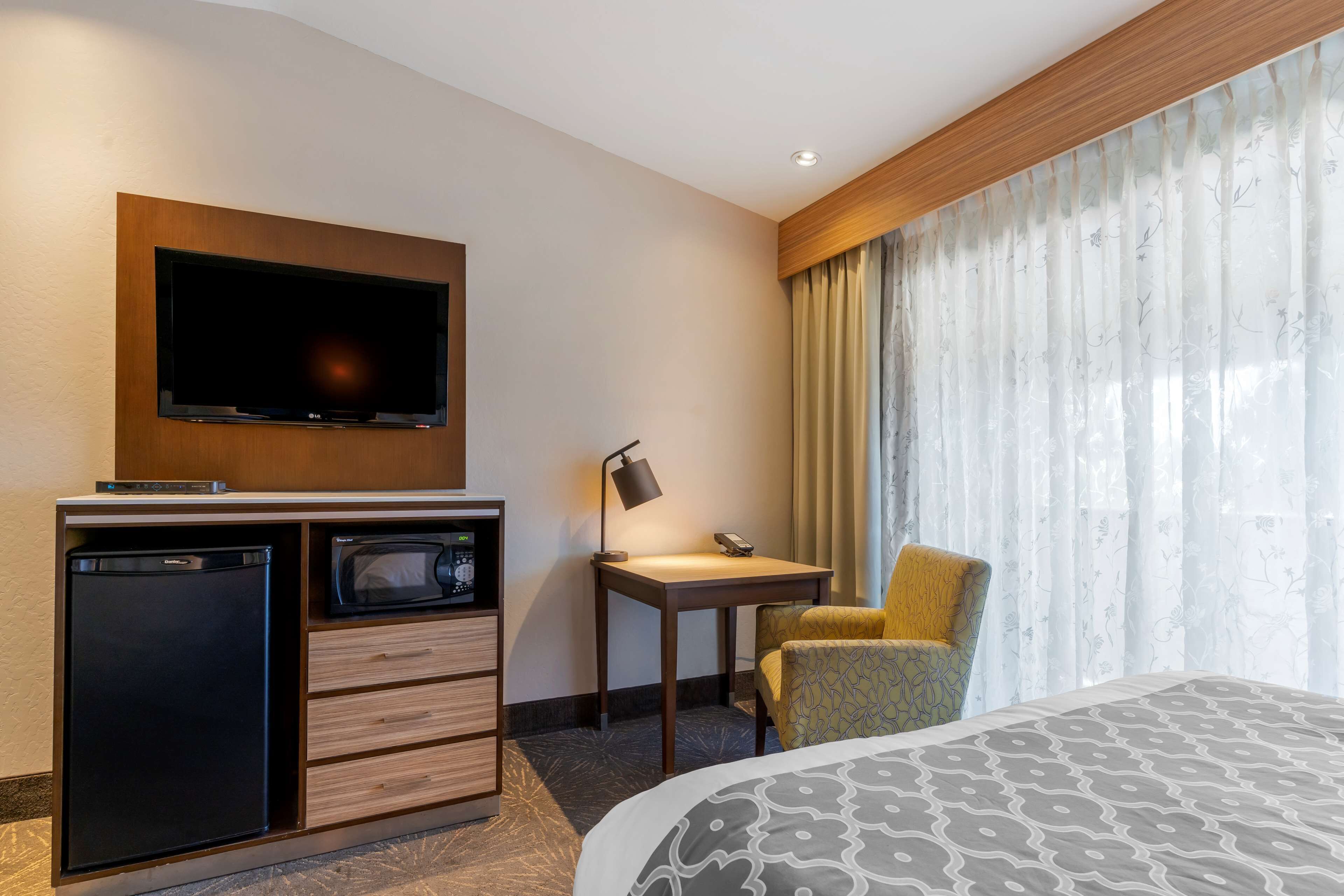 Une chambre d’hôtel comprenant un lit, un téléviseur fixé à un meuble en bois, un petit bureau avec une lampe, une chaise et un mini-bar.