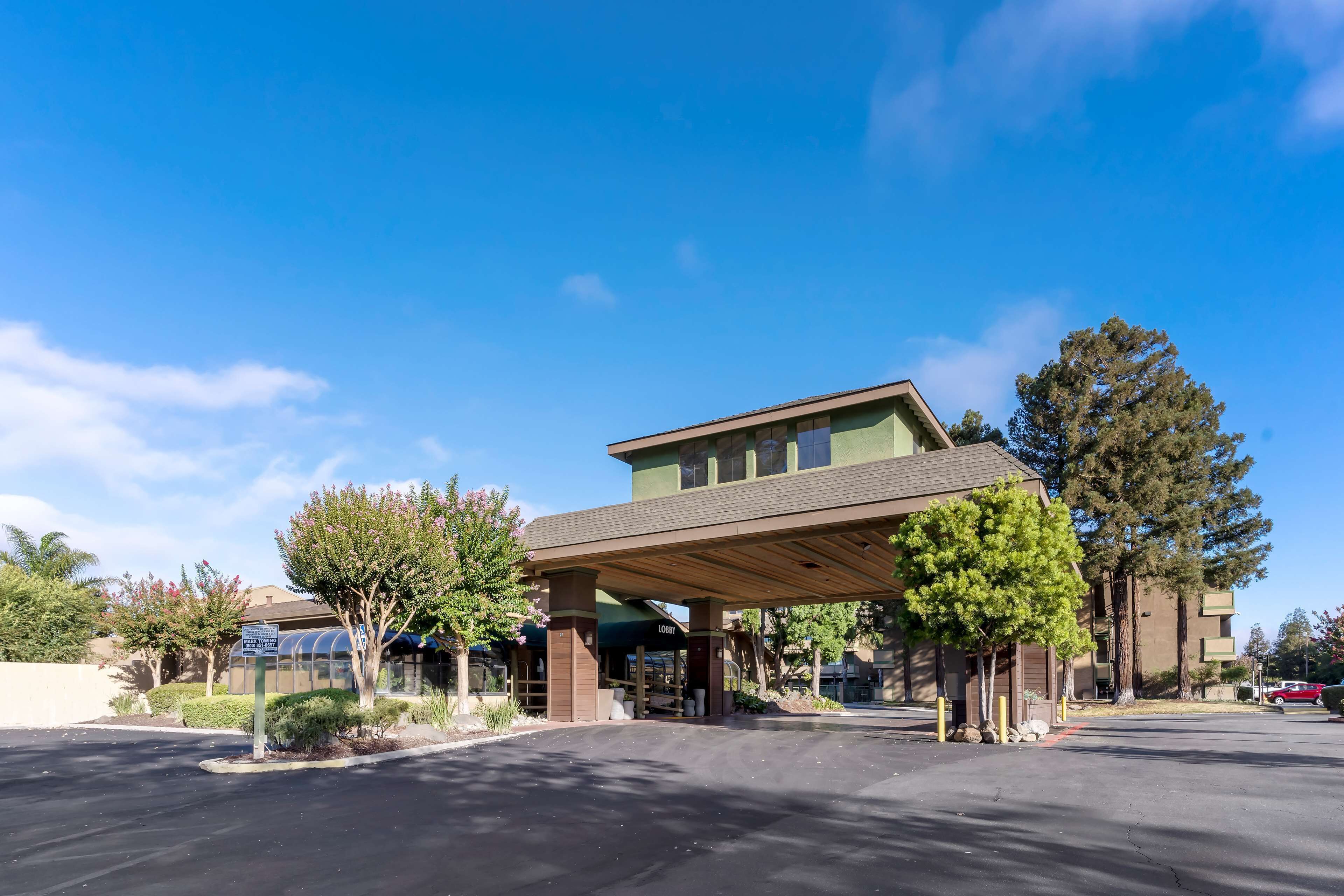 A building with a covered entrance, a parking lot, and surrounding trees.