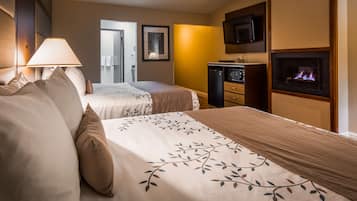 A hotel room with two beds, a TV, a fireplace, and a desk with a lamp.