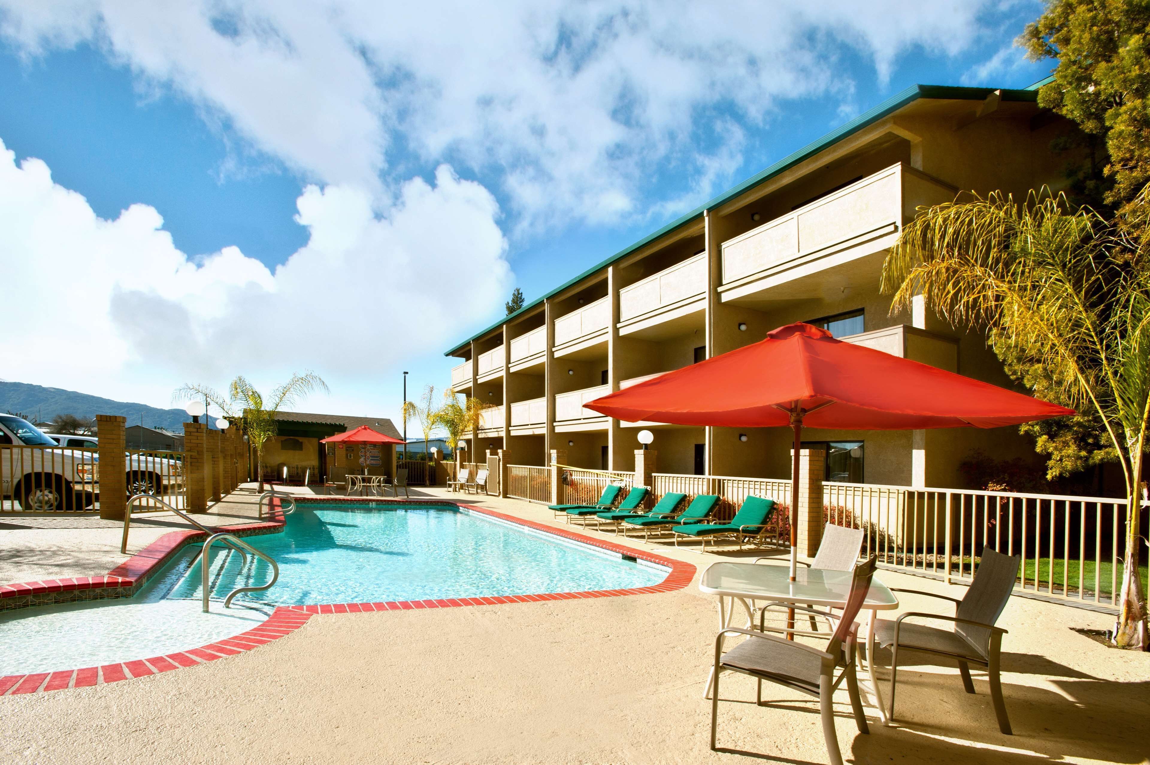 Une piscine avec des chaises longues et des parasols, un bâtiment doté de balcons et un ciel dégagé.