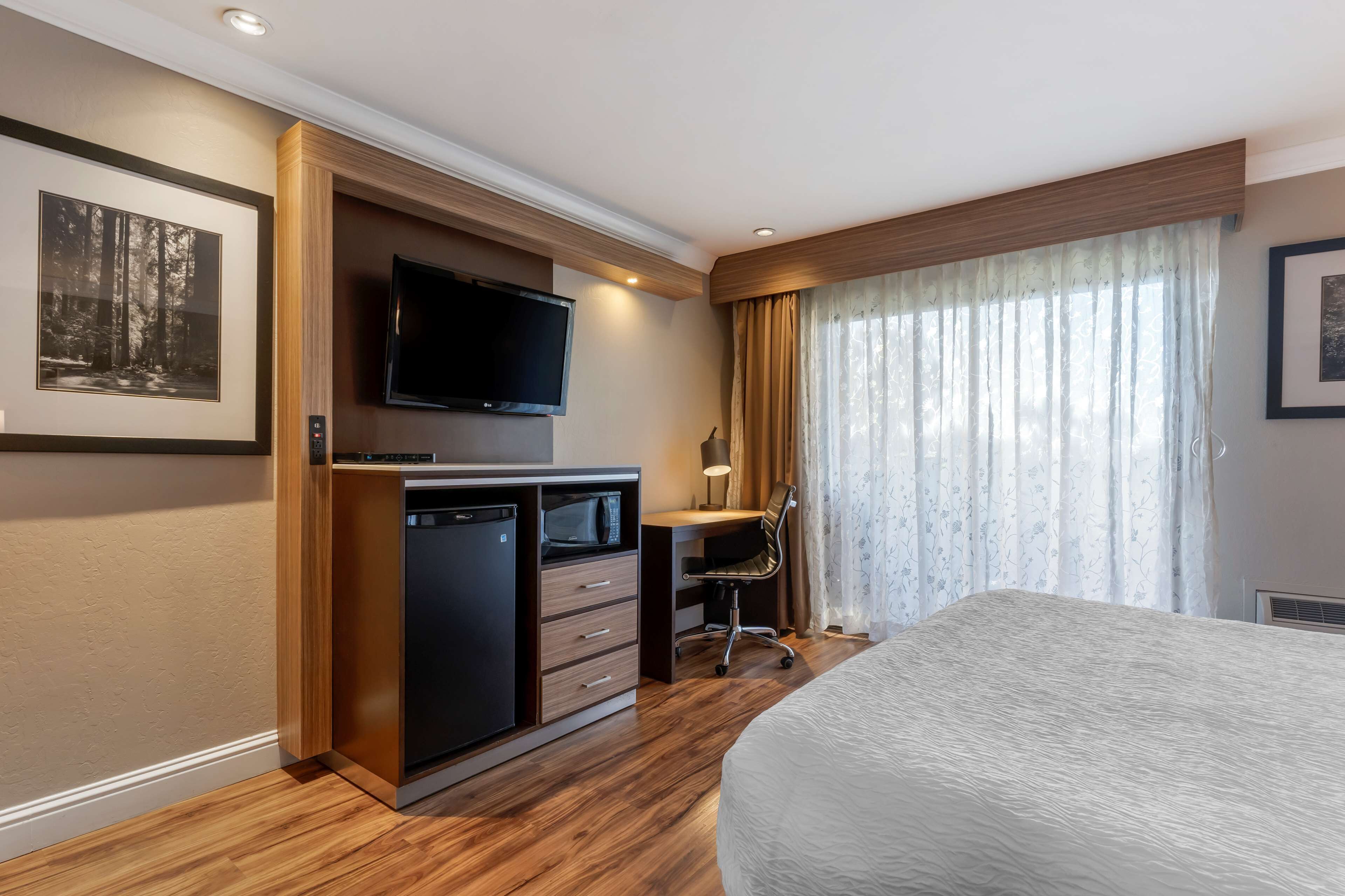 A hotel room with a bed, a desk with a chair, a television, and a wardrobe.