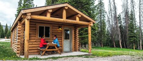 A wooden cabin with a porch, a door, and a window.