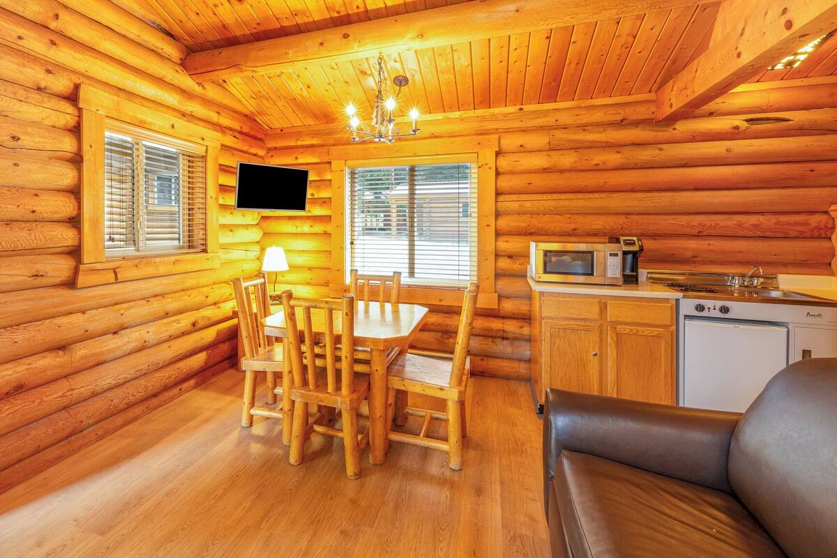 A cozy log cabin interior with a dining area, a kitchen with appliances, and a seating area.