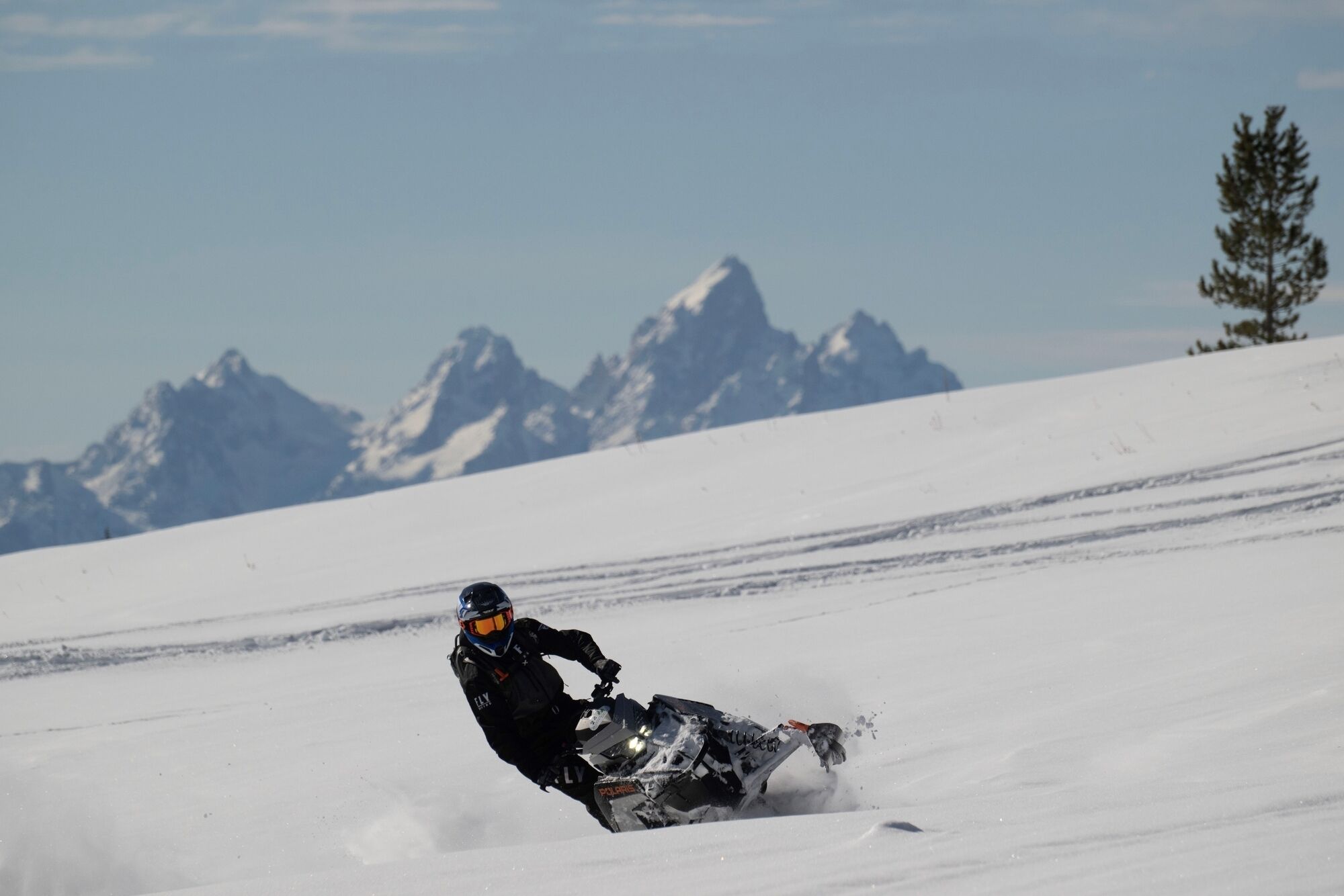 Une personne conduisant une motoneige sur une pente enneigée, avec une chaîne de montagnes en arrière-plan.