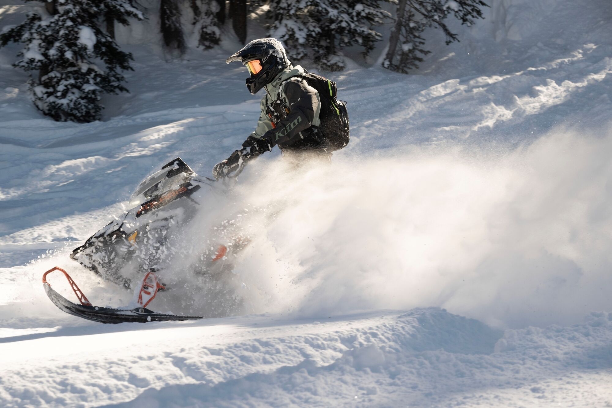 A person snowmobiling on a snowy trail with trees in the background.
