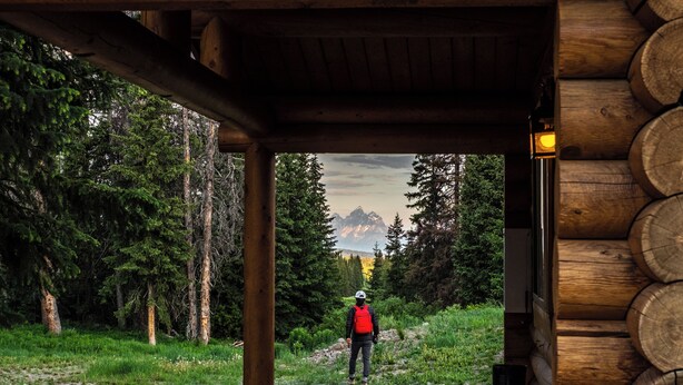 A wooden cabin with a view of a forest and mountains.