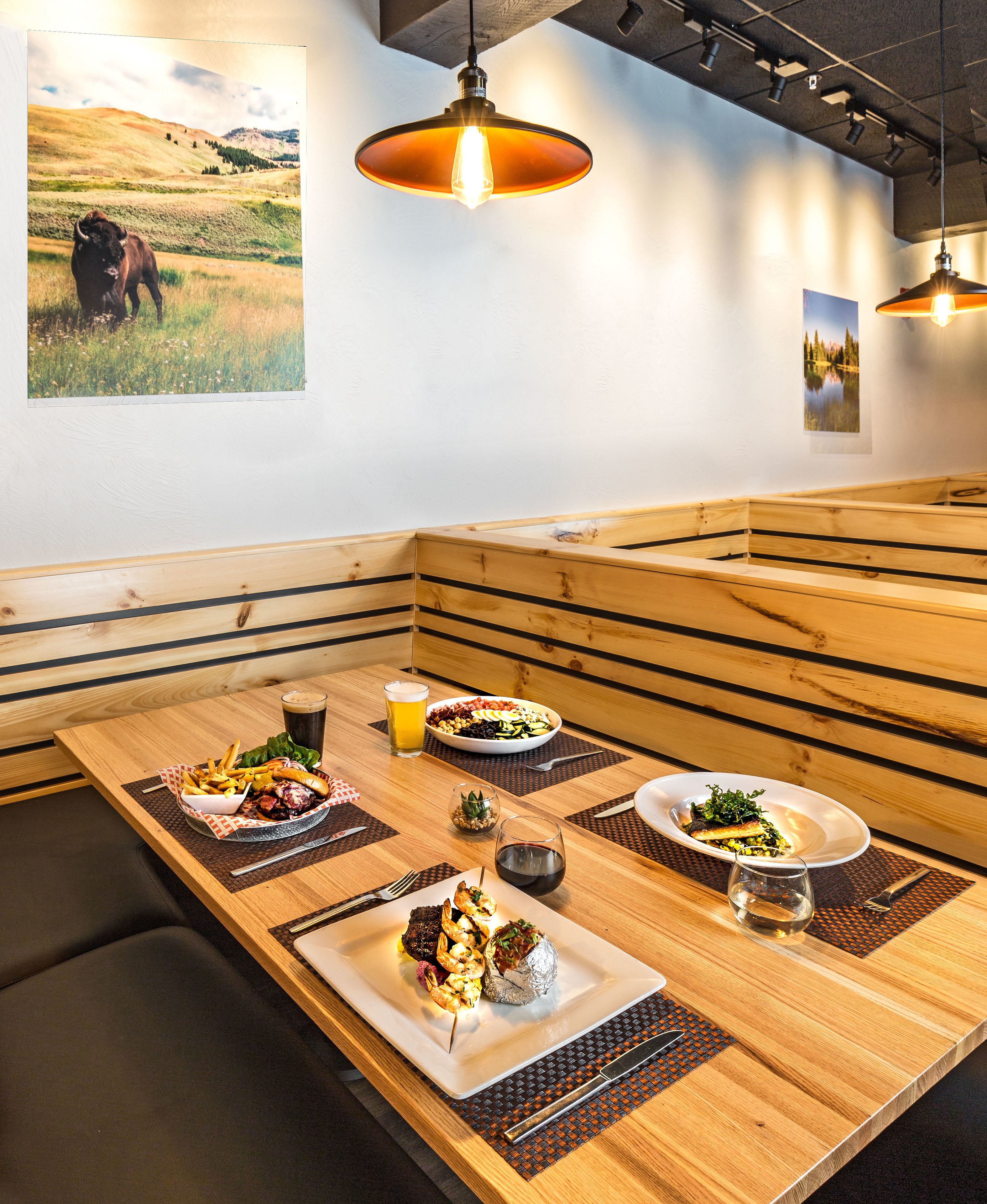 A restaurant with a wooden table set for a meal, including plates of food, drinks, and a bowl of salad.