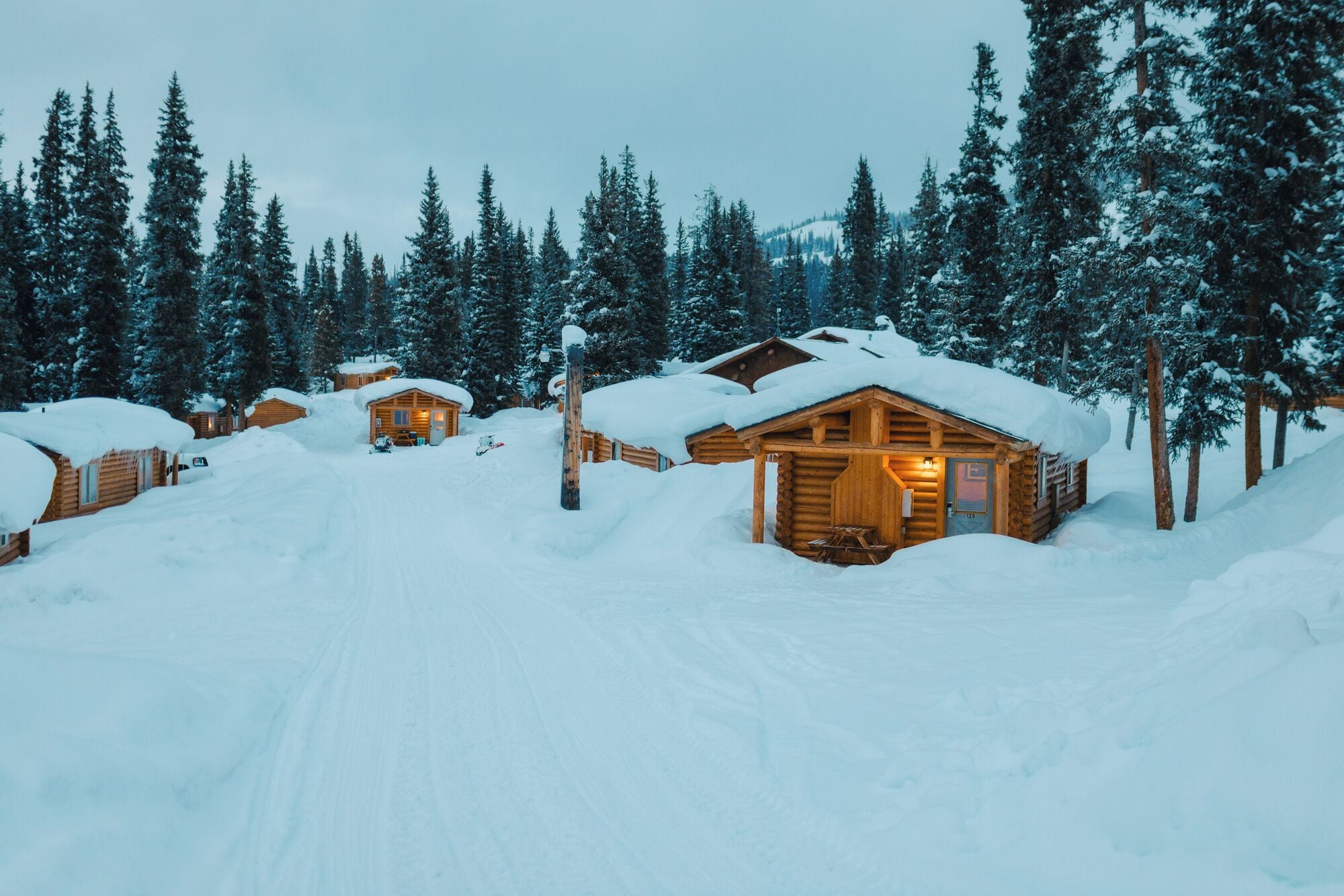 A snow-covered lodge with multiple cabins, surrounded by tall pine trees.